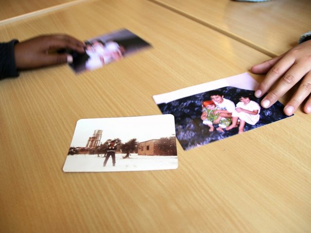 Händer som lägger fram tre fotografier på barn på bordet.